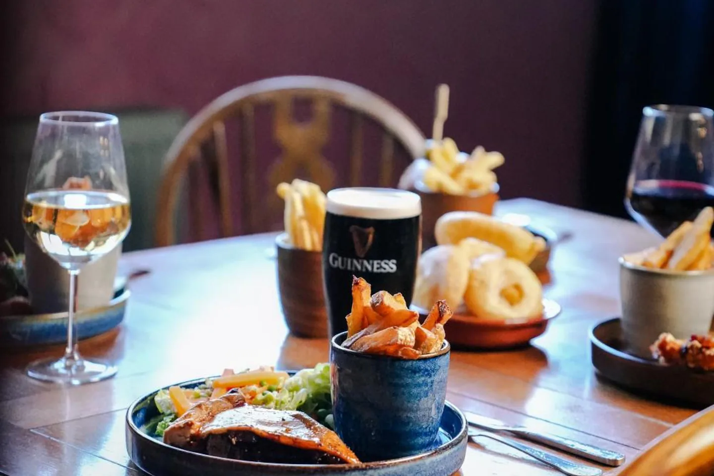 A laid table in the pub — a pie with chips, onion rings, a glass of stout and two glasses of wine