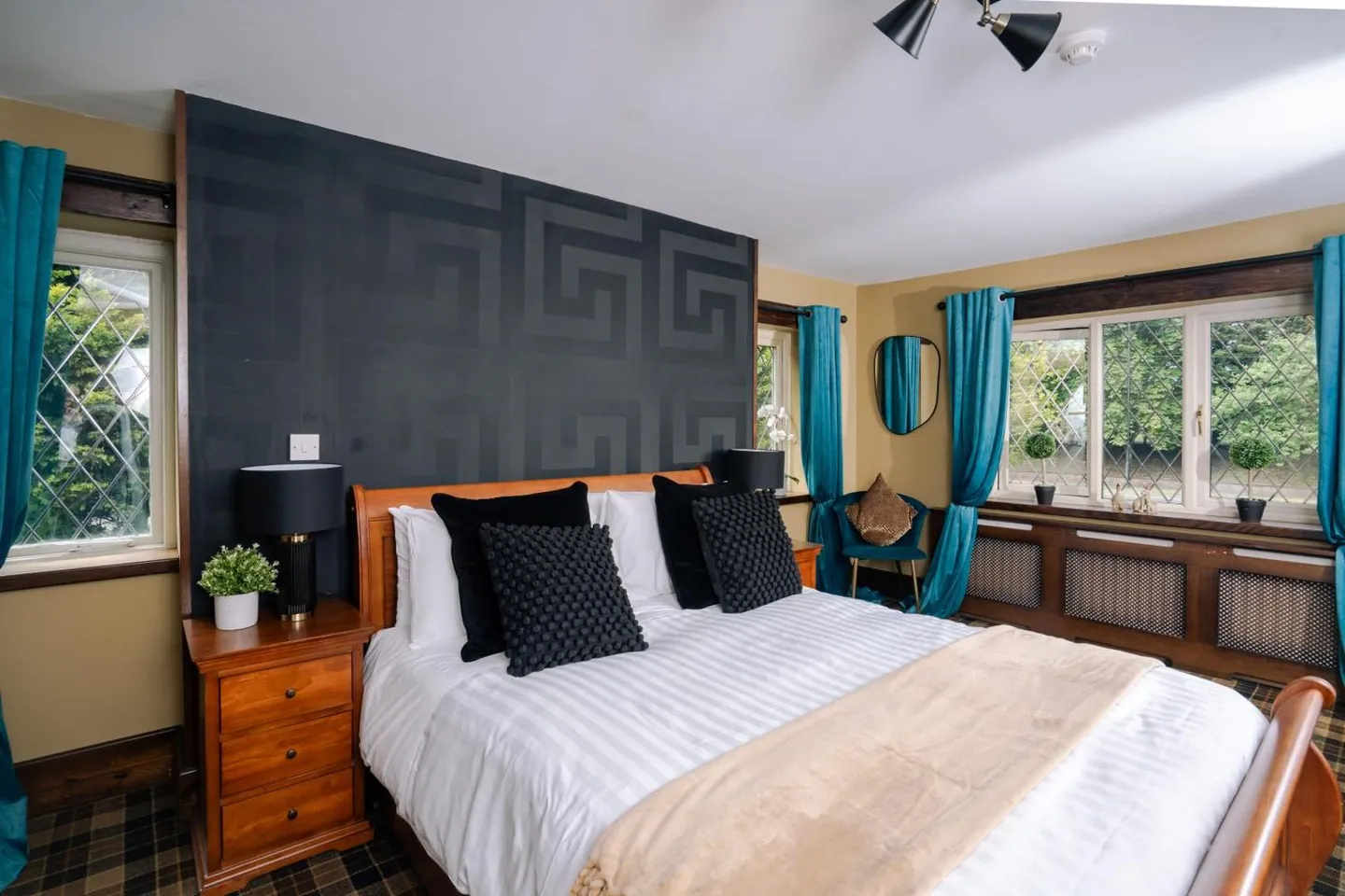 A double bed against a dark patterned feature wall, with teal curtains at leaded windows on two sides