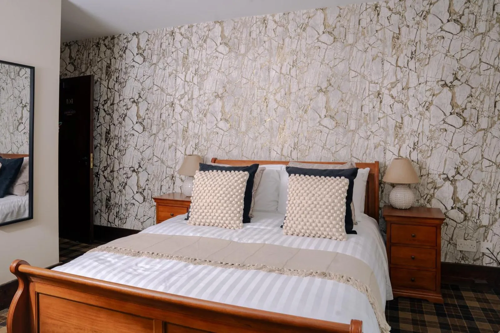 A double bed with a wooden sleigh frame against a stone-patterned wall, between two bedside tables