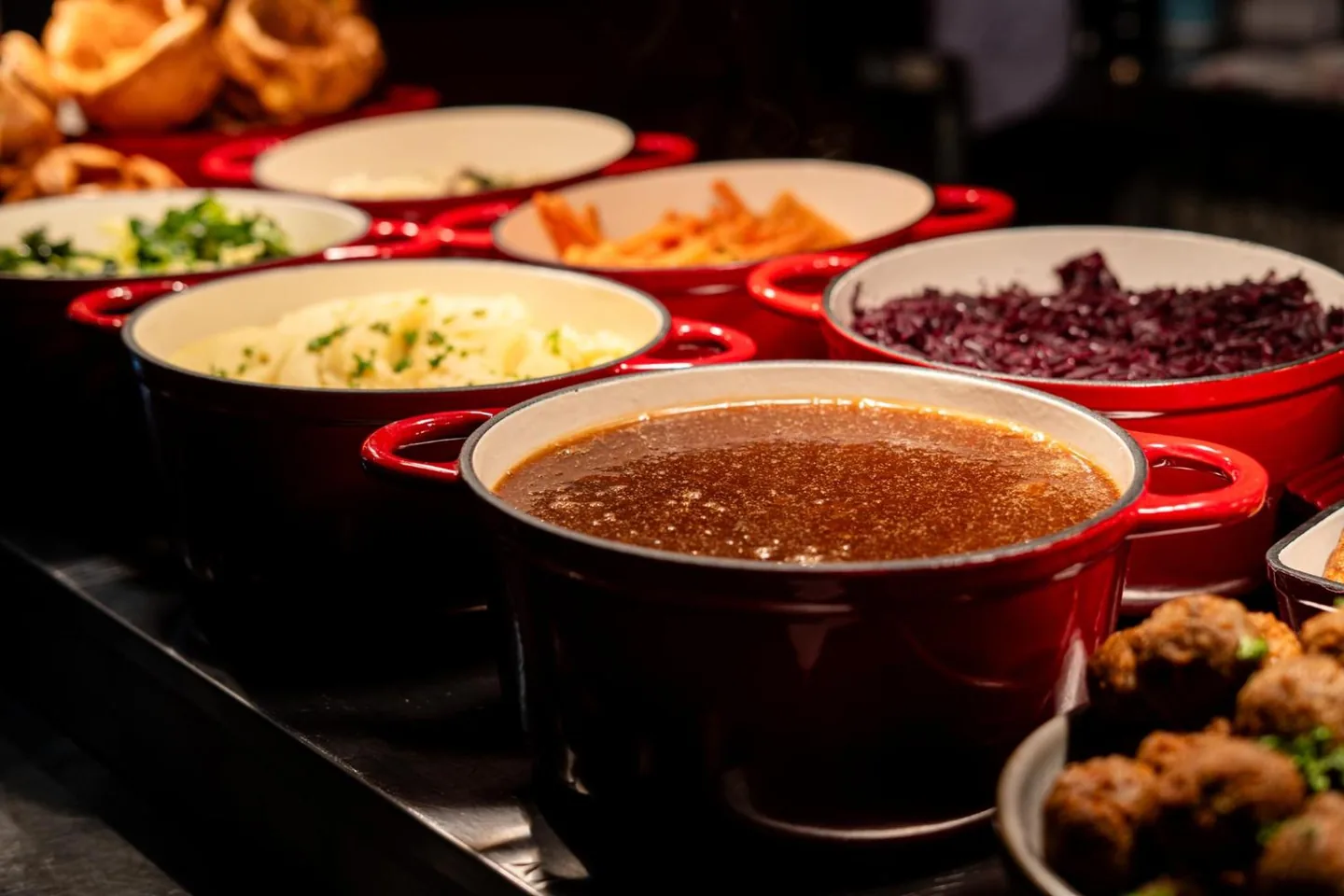 Sunday lunch being served — mash, greens, red cabbage, roast potatoes and gravy in red pots