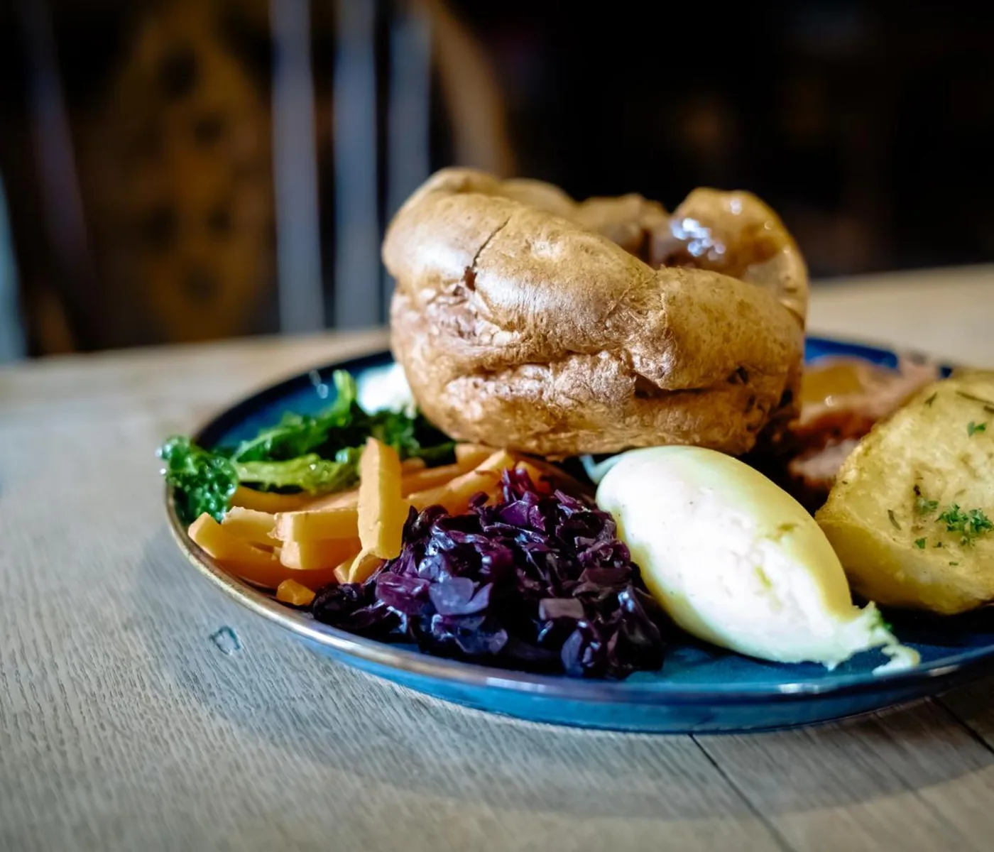 A plated Sunday roast — Yorkshire pudding, roast potato, red cabbage, mash, carrots and greens on a blue plate