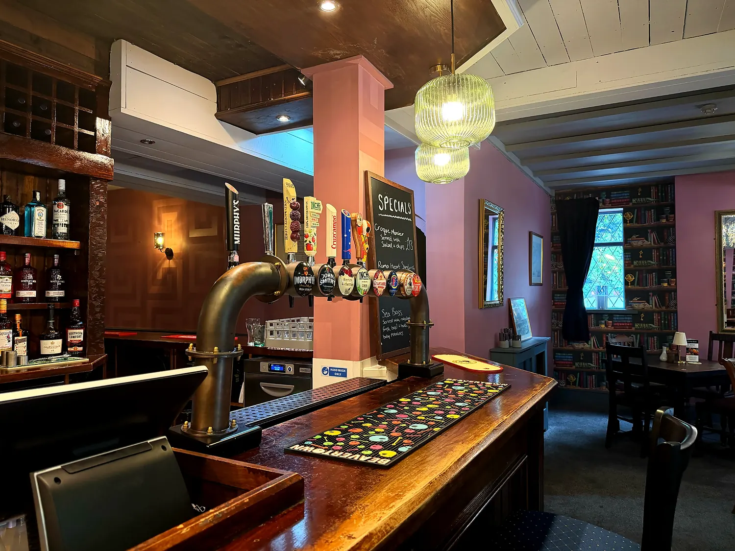 The bar at The Mayflower — brass taps, a specials board and glass pendant lights, with the dining room beyond